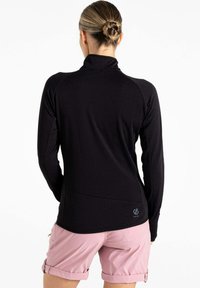 Schwarz Langarmoberteil mit hohem Kragen und taillierter Passform; Details umfassen ein Logo am Saum und eine glatte, dehnbare Textur. Rosa Shorts sind sichtbar.