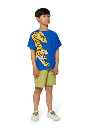 T-shirt en coton bleu avec un grand motif de tigre jaune et noir, associé à un short vert et des baskets blanches avec des accents de tigre.