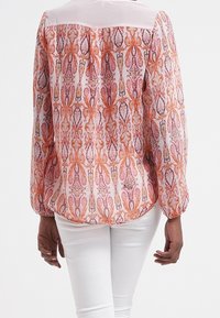 Blus med långa ärmar som har ett mönster i rosa och orange paisley, med en enhetlig ljusrosa ok och mjuka veck i ryggen.