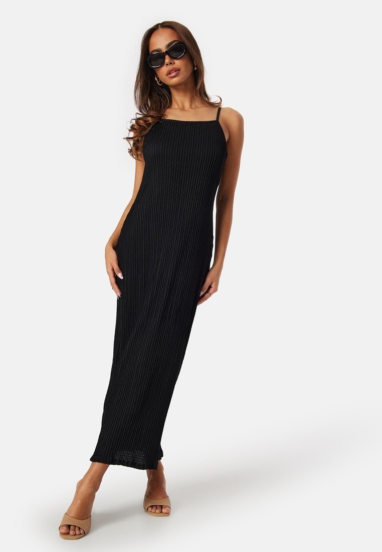 Maxi dress nera in maglia con texture a costine, spalline sottili e silhouette dritta. Indossata con occhiali da sole neri e tacchi beige.