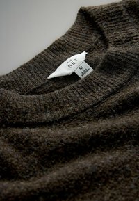 Hnědý pletený svetr s žebrovanou texturou a kulatým výstřihem. Obsahuje štítek s nápisem „THE SET“ a velikostí „M“. Látka působí měkce a teple.
