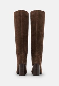 Bottes en daim marron jusqu'au genou avec un bout rond, présentant un heel bloc en bois poli et une texture lisse. Design minimaliste, sans embellissements.