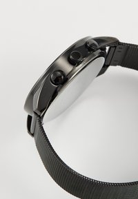 Schwarze Uhr mit einem Metall-Mesh-Armband, runden Gehäuse und zwei Druckknöpfen. Glatte Oberfläche des Gehäuses und Armbands mit minimaler Gestaltung.