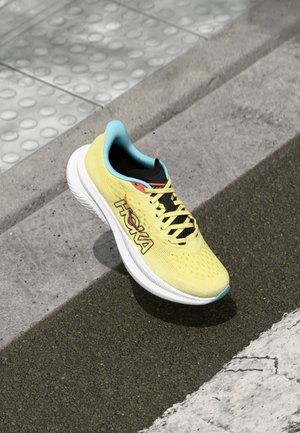 Yellow running shoe with breathable mesh upper, black laces, and blue accents. Features a thick white midsole and textured outsole.