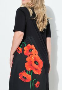 Schwarzes Kleid mit kurzen Ärmeln und fließendem Design. Verfügt über große, lebendige orangefarbene Mohnblumenmuster entlang der Seite vor einem schwarzen Hintergrund.