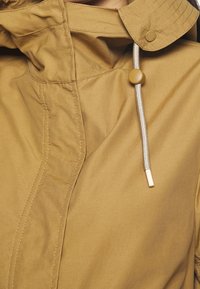 Beżowa lekka kurtka z zamkiem błyskawicznym, kapturem ze ściągaczem i kremowymi akcentami. Charakteryzuje się widocznymi szwami i teksturowaną tkaniną.