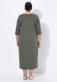 Olivgrön klänning i knälängd med trekvartslånga ärmar och resår i midjan. Slät textur; bakifrån visar den en minimalistisk design.