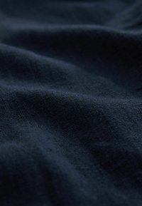 Tissu bleu marine foncé avec une surface douce, légèrement texturée, et des plis doux créant des ombres subtiles et des reflets.