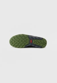Trailrunning-Schuhsohle mit grünem Gummiunterteil und multidirektionalen Stollen für Grip, grauen Akzenten und rotem Branding-Element.