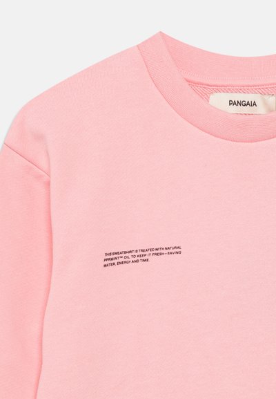 Rosa genser med rund hals, med en myk tekstur og små svarte tekstdetaljer som gir vaskeanvisninger foran.