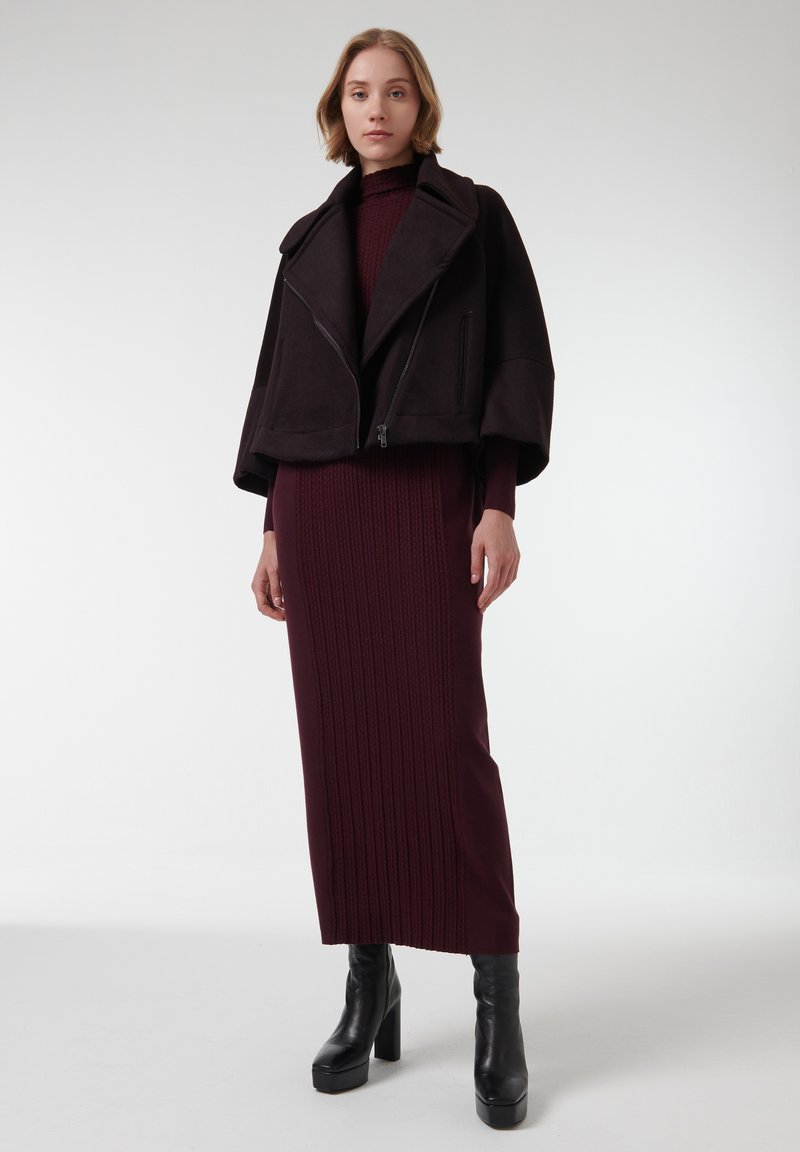 Chaqueta negra corta con mangas anchas sobre un vestido burdeos con relieve, combinada con botas de tobillo negras con plataforma. Texturas suaves.