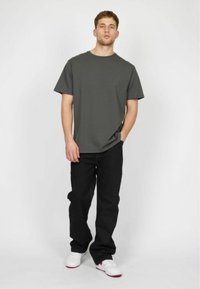 Grå crew-neck t-shirt med korte ærmer, parret med løse sorte jeans og hvide sneakers med røde detaljer. Enkelt design, ingen mønstre.
