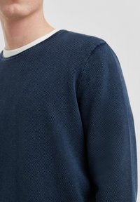 Marineblauwe trui van textiel met structuur, ronde halslijn met een witte afwerking en zichtbare stikdetails op de mouwen.
