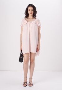 Šviesiai rožinė, laisvai krentanti suknelė su trumpais rankovėmis ir volanų detalėmis. Derinama su mažąja juoda rankine ir juodais dirželiais sandalais, iki kelių ilgio.