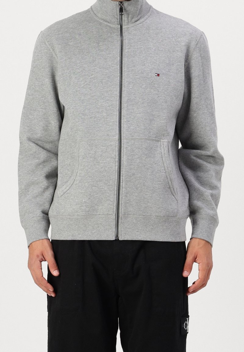 Grauer Sweatshirt zum Reißverschluss aus Baumwollmischung mit hohem Kragen, zwei Fronttaschen und einem kleinen Logoakzent auf der Brust. Glatte Textur.