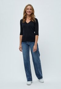 Schwarzes, geripptes Strickoberteil mit V-Ausschnitt und Dreiviertelärmel. Tragen mit hellblauen, weit geschnittenen Jeans und weißen Sneakers vor einem schlichten Hintergrund.
