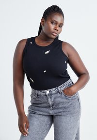 Black ribbed tank top with small floral embroidery details; paired with high-waisted, light gray denim jeans.