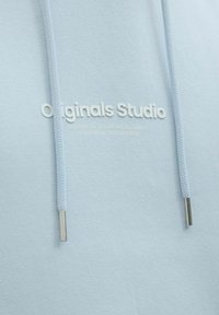 Jasnoniebieska bluza z kapturem z teksturowanej tkaniny, z regulowanym sznurkiem z metalowymi końcówkami i wytłoczonym białym logo z napisem "Originals Studio."
