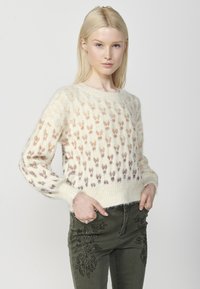 Pulover din lână în nuanță crem, cu un model texturat de frunze colorate mici; guler rotund și croială ușor scurtă. Asortat cu blugi verzi măslinii.