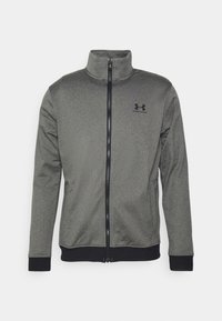 Chaqueta gris con cremallera y cuello alto, hecha de una tela texturizada. Presenta detalles en negro y un logotipo sutil en la parte superior izquierda.