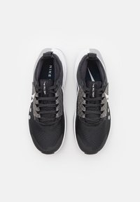 Scarpe da ginnastica nere con tomaia in rete, lacci testurizzati e accenti, dettagli grigi sui lati e suola bianca. Logo Nike visibile.