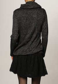 Svart och grå stickad tröja med en variant av hög krage, med avslappnad passform och strukturmönster, kombinerad med en svart spetskjol.