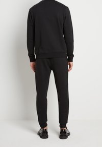 Zwarte sweatshirt en bijpassende sweatpants, beide gemaakt van een zacht materiaal. Het ontwerp heeft geribbelde boorden en een relaxte pasvorm.