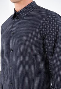 Chemise marine à boutons avec un motif géométrique de petits diamants blancs et rouges, en tissu lisse avec un col classique.