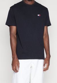 Czarny bawełniany t-shirt z okrągłym dekoltem, krótkimi rękawami oraz małym haftowanym logo w kolorach czerwonym, białym i niebieskim na lewej piersi.