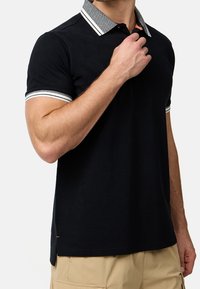 Schwarzes Poloshirt mit einem strukturierten grauen Kragen und gestreiften Akzenten. Verfügt über kurze Ärmel und einen seitlichen Schlitz am Saum für mehr Bewegungsfreiheit.