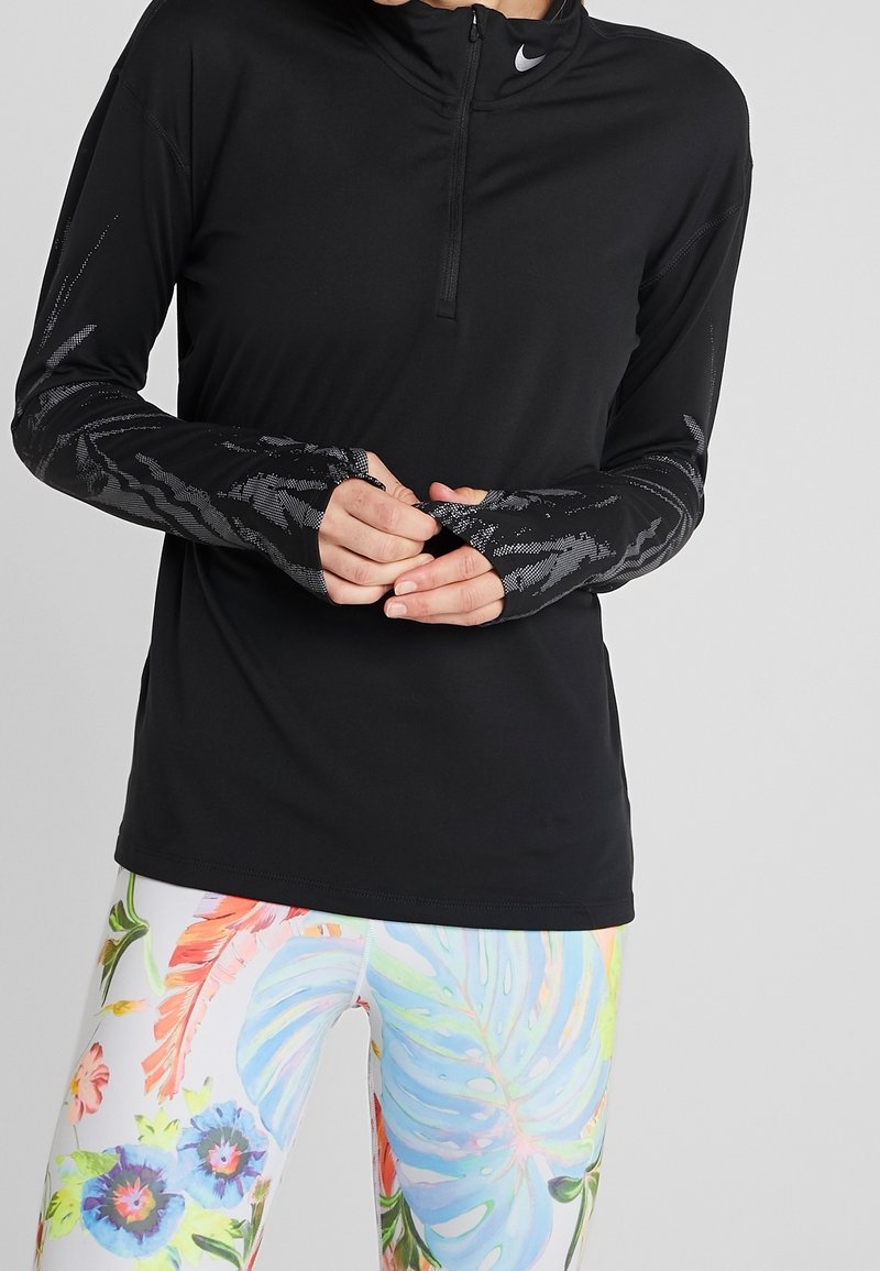 Osoba nosząca czarną, długą sportową bluzę z otworami na kciuki oraz kolorowe legginsy z dużymi, pastelowymi wzorami kwiatowymi.