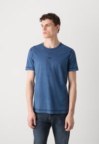 Μπλε βαμβακερό T-shirt με γυρό λαιμό, κοντά μανίκια και μια διακριτική λογότυπο στο στήθος. Λείο ύφασμα, casual στυλ. Συνδυάζεται με τζιν παντελόνι.