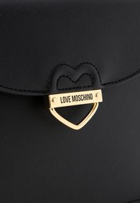 Black fabric handbag featuring a gold heart-shaped clasp with "LOVE MOSCHINO" engraved. Distinct textured surface and stitched heart detail.