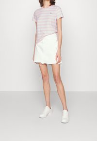 Rosa och vita randiga t-shirt, avslappnad passform, kombinerad med en vit denimkjol med fransad nederkant. Modellen bär vita sneakers.