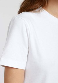 T-shirt bianco in cotone con scollatura rotonda e maniche corte. Il tessuto ha una consistenza morbida e liscia con una leggera elasticità.