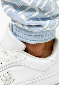 Light blue sweatpants with white lettering and elastic cuffs paired with a white sneaker featuring a crown design on the side.