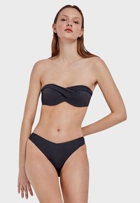 Crni bandeau bikinij gornji dio s uvijenim dizajnom i teksturiranim materijalom. Nisko rasječeni odgovarajući bikini donji dio s v-oblikovanim izrezom. Glatka završna obrada.