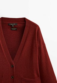 Punainen villa-kashmir-cardigan, jossa on V-pääntie, kaksi etutaskua ja nappikiinnitys. Pehmeä rakenne, rento istuvuus ja klassinen muotoilu.