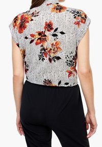 Blusa a maniche corte in tessuto leggero, caratterizzata da un motivo a righe verticali bianche e nere con una stampa floreale colorata in rosso, arancione e nero.