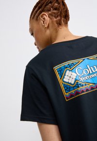 Sort bomulds T-shirt med et farverigt geometrisk grafik på ryggen med teksten "Colur Sportswear." Rund halsudskæring og korte ærmer.