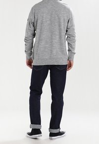 Camisa gris de manga larga con costuras laterales, combinada con jeans azul oscuro y zapatillas negras. La camisa tiene una tela ligeramente texturizada.