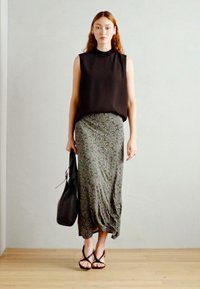 Top negro sin mangas, falda midi verde estampada, bolso negro y sandalias negras con tiras. Tela suave, diseño fluido y apariencia en capas.