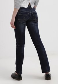 Jeans de mezclilla oscura con corte recto, que presentan bolsillos traseros y detalles de costura visibles. La textura es suave con un ligero desgaste.