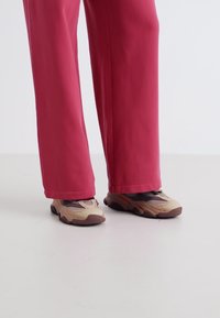 Des chaussures de sport avec une combinaison de couleurs beige et marron, tige en mesh et semelle en caoutchouc épaisse, accompagnées d'un pantalon rose ample.