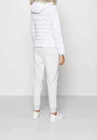 Biała kurtka puchowa z kapturem z sztucznym futrem, w połączeniu z jasnoszarymi dresami i białymi sneakersami. Gładka, wypełniona tekstura i swobodny krój.