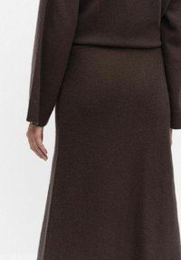 Ruskea neulottu hame, jossa on pehmeä rakenne, flare-mallinen design ja sivuaukot liikkumisen helpottamiseksi.