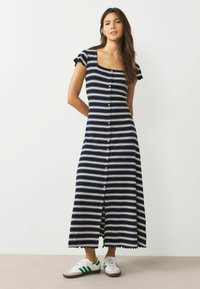 Námořnické pruhované šaty s krátkými volánovými rukávy, čtvercovým výstřihem a knoflíkovým zapínáním. Doplněné o bílé tenisky se zelenými pruhy.