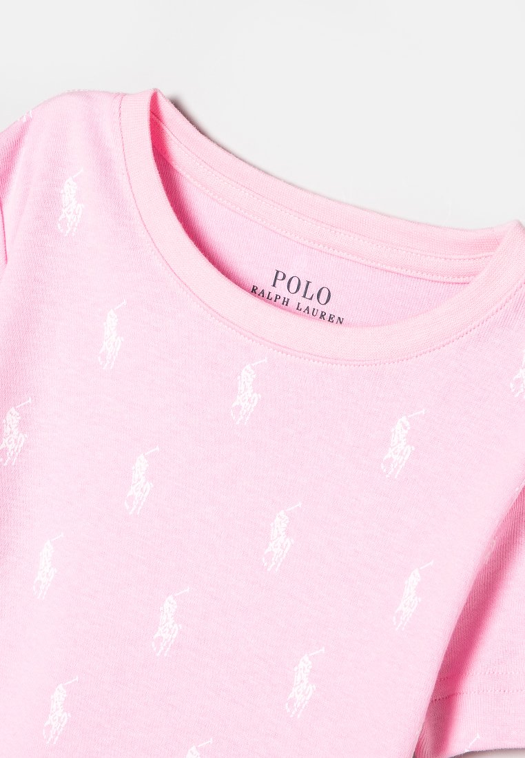 Jasnoróżowa koszulka Polo Ralph Lauren z białymi logo polo gracza rozsianymi po tkaninie oraz okrągłym dekoltem.