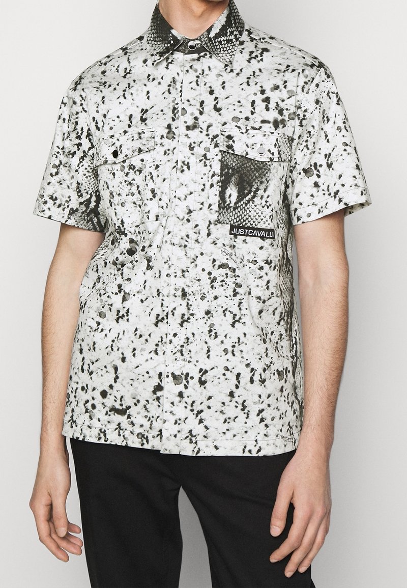 Camicia a maniche corte bianca con pattern a macchie nere, dotata di tasca con stampa di serpente e etichetta del logo. Collo button-down, vestibilità comoda.