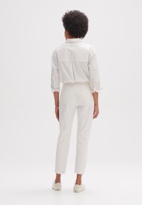 Vit skjorta med krage och uppvikta ärmar kombinerad med vita högmidjade byxor. Byxorna har en slät yta och bakfickor.